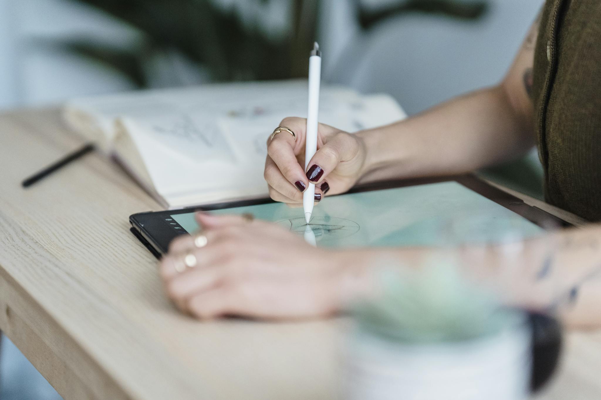 Crop unrecognizable female designer using tablet and stylus for drawing sketches on wooden table